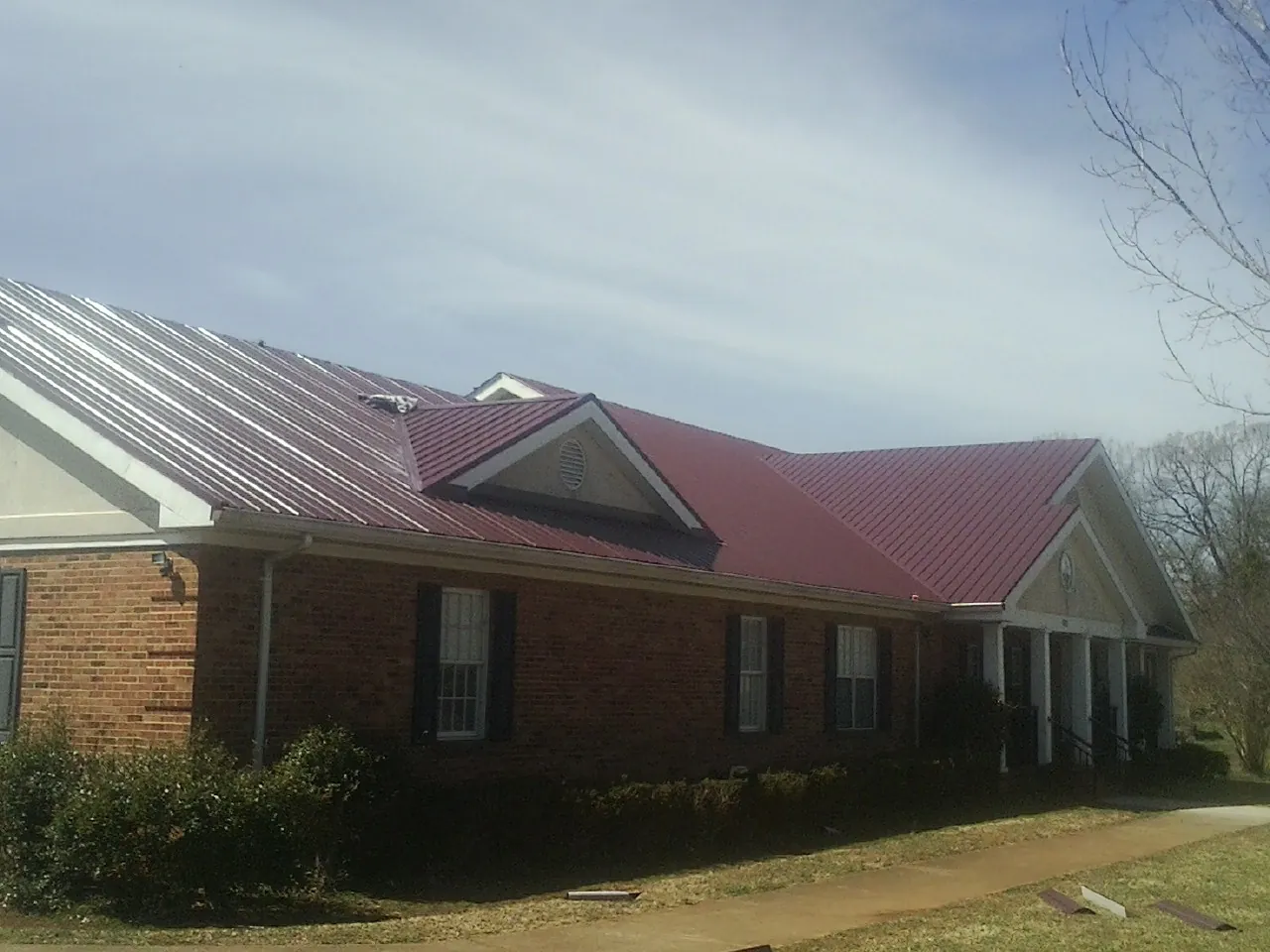 Red metal roof with gabled entries on a long brick building, from a Hail Damage Roof Repair job in Shoemakersville