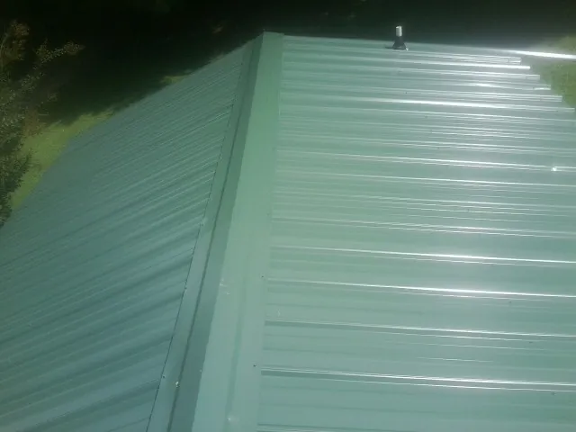 New green metal panels meeting at the ridge of a roof — Flat Roof Repair work by our crew in Shoemakersville
