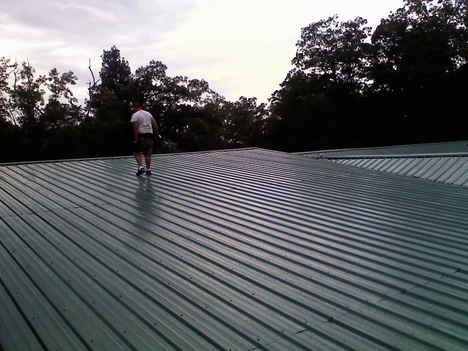 Roofer walking a wide expanse of new green metal roofing in Shoemakersville