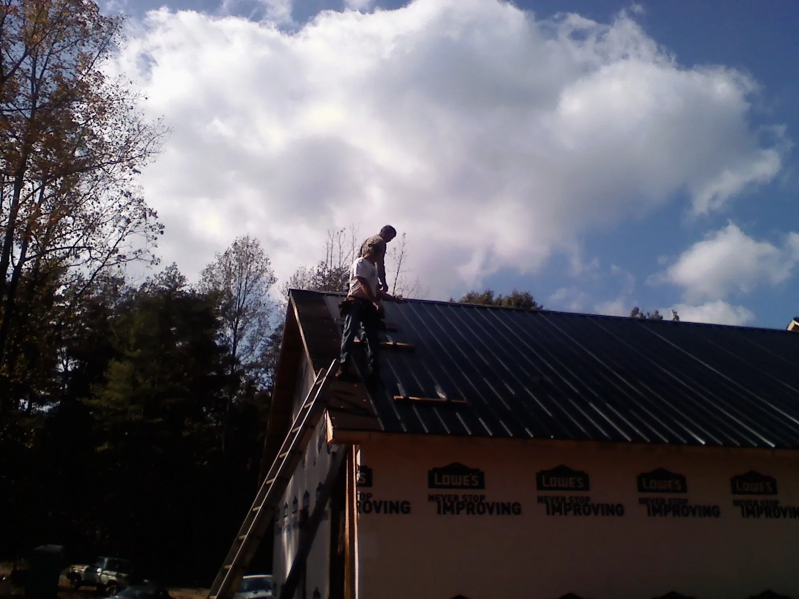 Roofer fastening dark metal panels high against a cloudy sky, from a Roof Inspection job in Shoemakersville