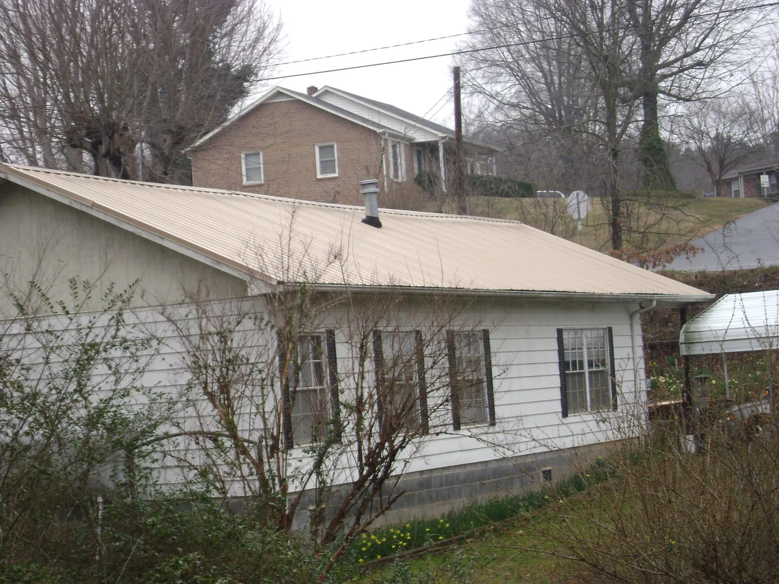 Tan metal roof on a white sided house set into a hillside — Commercial Roofing by Roofing Brothers in Shoemakersville